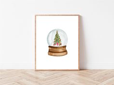 a snow globe with a christmas tree in it on a wooden table next to a white wall