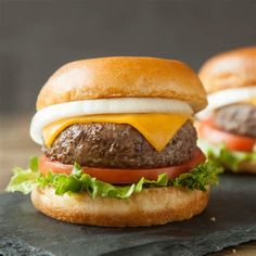 two hamburgers with cheese and lettuce on them sitting on a slate board