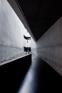 a black and white photo of a bench in a dark room with light coming from the ceiling