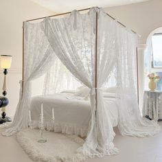 a white bed sitting in a bedroom next to a window with curtains on top of it