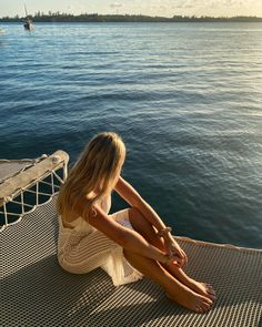 a woman sitting on top of a boat in the ocean with her legs crossed and looking at the water