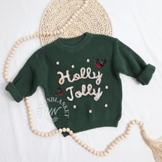 a green sweater with the words holly jolly written on it next to a tassel