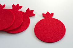 four red felt coasters sitting next to each other on a white surface with the shape of a pomegranate