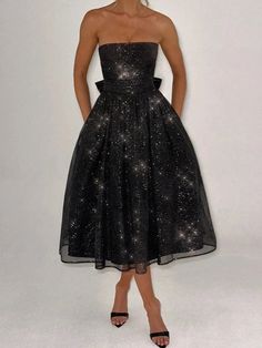 a woman in a strapless black dress poses for the camera with her hands on her hips