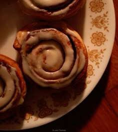 three cinnamon rolls on a plate with icing drizzled over them and sitting on a table