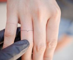 a woman's hand with a small heart tattoo on her left ring finger,