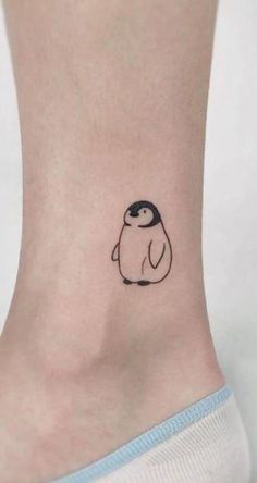 a small penguin tattoo on the side of a woman's ankle, with black ink