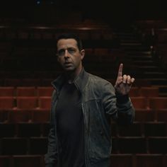 a man standing in front of an auditorium holding his hand up to the camera and making a peace sign