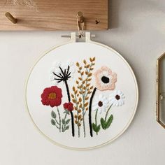 a white wall hanging with flowers on it and a wooden frame above the embroidery hoop