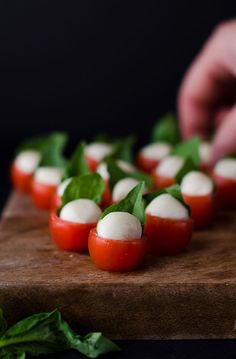 small tomatoes and mozzarella on a wooden cutting board with basil sprigs