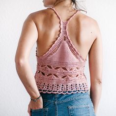 a woman wearing a pink crochet top and blue jeans is looking at the wall