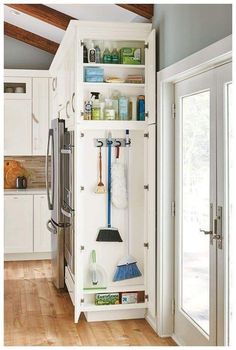 a kitchen with white cabinets and shelves filled with cleaning supplies on top of wooden floors