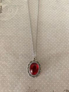 "This pretty oval shaped necklace in tibetan silver and red has an intricately designed edging with a red crystal center stone. Pendant measures 1\" L X 7/8\" W and is on an 18\" chain. ★ Want to see more? Please visit my shop at: https://www.etsy.com/shop/DesignsByPeg" Red And Silver Necklace, Silver Necklace With Red Stone, Necklace Red, Dark Red Jewelry, Red Jewellery, Red Pendant Jewelry With Stones, Red Vintage Necklaces With Natural Stones, Vintage Red Gemstone Necklace, Red Crystal Pendant Necklaces