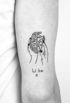 a black and white photo of two hands holding a brain tattoo on the left inner arm