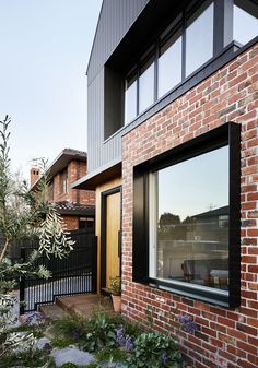 a brick house with an open window on the side and plants in the foreground