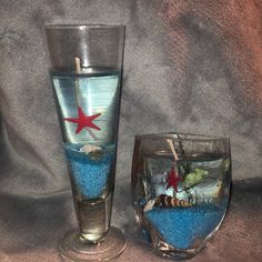 two glass vases with blue sand and starfish in them, one is filled with water