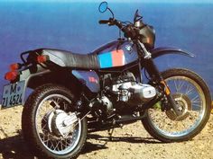 a motorcycle parked on the side of a hill next to the ocean in front of a sign