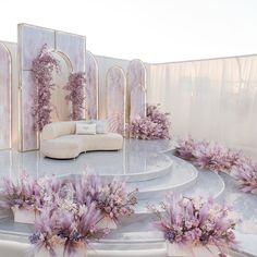 a white couch sitting on top of a stage covered in purple flowers and greenery