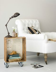 a white chair sitting next to a table with a lamp and books on top of it