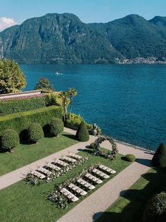 an aerial view of a wedding setup on the lawn next to water with mountains in the background