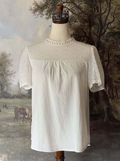 A charming historically inspired blouse that can be used in outfits ranging from the Edwardian era to the 1960's! This piece features a dainty eyelet lace yoke, scalloped lace mock-neck collar, short sleeves, and a gathered bodice. A versatile choice for building your historical wardrobe. This piece is part of our sustainable Secondhand, Vintage, and Upcycled Collection, and thus stock is limited to one! Sizing: Tag size XL, Fits like an XL.Bust up to 44 Inches / 110 CentimetersWaist up to 44 Inches / 110 CentimetersLength - 24.5 / 62 CentimetersSleeve Length - 8 / 22 CentimetersSleeve Width - 8 Inches / 22 Centimeters Condition: B | Some feeling of use, no major flaws. Materials: 100% Polyester synthetic "linen." The Edwardian Era, Gathered Bodice, Eyelet Blouse, Medieval Fashion, Rococo Style, Edwardian Fashion, Edwardian Era, Curated Vintage, Baroque Fashion