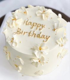 a birthday cake with white frosting and gold writing on the top that says happy birthday