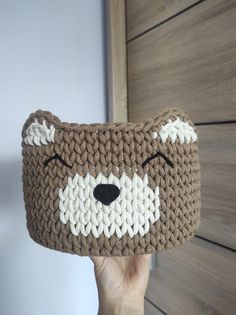 a hand holding up a brown and white crocheted bear head bag with eyes closed