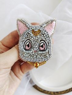 a hand holding a small cat brooch with pink eyes