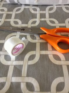 an orange pair of scissors sitting on top of a bed next to a roll of tape