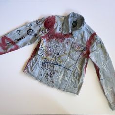 a jean jacket with graffiti all over it on a white surface, showing the back and sides