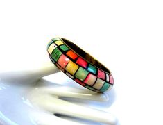 This colorful vintage bangle from the 60's features squares of dyed Mother of Pearl shell, done in candy-like hues and set against a black background. The band itself is brass and shows some wear on the interior, but is otherwise in excellent condition. It has an 8" inside circumference and is almost 1" in width. Each piece of jewelry comes carefully packed in a gift box for you to enjoy or give. Jewelry lots may be packed safely together. I am so excited to be sharing my jewelry with you! I sold thousands of pieces of vintage jewelry over a span of eight years on Ruby Lane, but I still have so much of it left. (Too much collecting and not enough selling!) It does me no good to have it sitting on my shelves, so I'm offering it at a great price. Don't let the price fool you, though, as it's Multicolor Retro Bracelet For Gift, Multicolor Retro Bracelet As Gift, Multicolor Retro Bracelets For Gift, Retro Multicolor Bracelets As Gift, Retro Multicolor Bracelets For Gift, Retro Multicolor Bangle Jewelry, Retro Multicolor Bangle Bracelets, Shell Mosaic, Brass Bangle