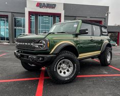 a green and black truck parked in front of a building with red stripes on it