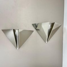 two metal triangles are hanging on the wall next to each other, one is upside down