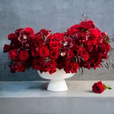 a white vase filled with red flowers on top of a table next to a gray wall