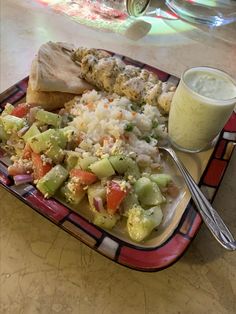 a plate with rice, meat and vegetables next to a glass of milk on a table