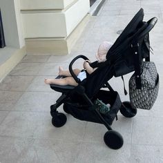 a baby in a stroller sitting on the ground next to a building and another person walking by