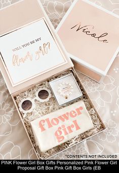 a pink flower girl gift box sits on a bed next to a card and some other items