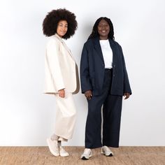 two women standing next to each other in front of a white wall and wooden floor