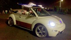 a white car with two people in it driving down the street at night, near an amusement park