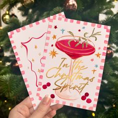 two handmade christmas cards in front of a christmas tree with gold foil lettering on them