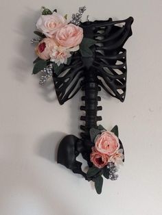 a skeleton with flowers attached to it's back is hanging on the wall in front of a white wall