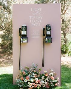 two old fashioned telephones sitting on top of a pink sign with flowers in the foreground