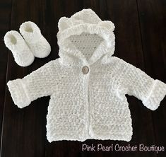 a white crocheted baby jacket and booties on a wooden floor