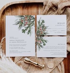 the wedding stationery is laid out on a wooden tray with greenery and red berries