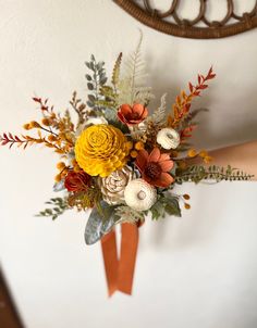 a bouquet of flowers is hanging on the wall by someone's hand with an orange ribbon