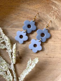 three blue flower shaped earrings sitting on top of a wooden table next to white flowers