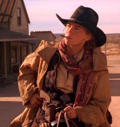 a woman wearing a cowboy hat and scarf sitting on a horse in front of a house