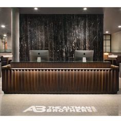 the front desk of an office with two computers on it's sides and a black wall behind it