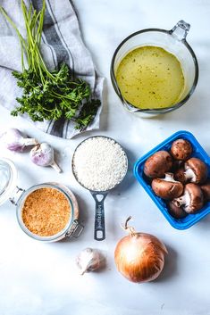 ingredients to make mushroom soup laid out on a white counter top, including onions, garlic, parsley and seasoning