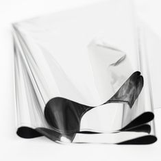 black and white photograph of abstract shapes on a white table top, with one curved piece of glass in the foreground